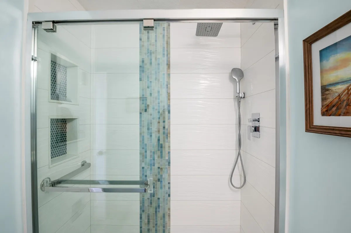 A close-up of a glass shower door with colorful tile accent and a sleek shower head, creating a refreshing and calming spa-like atmosphere ideal for unwinding after a day outdoors.