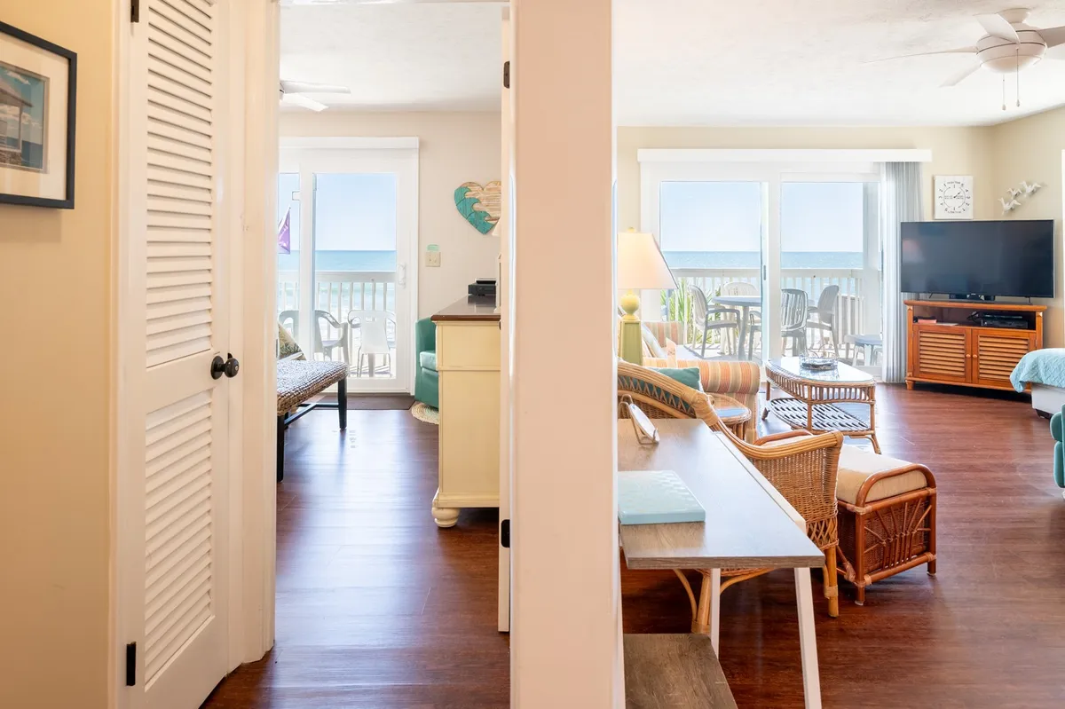 A cheerful living space with comfortable seating, colorful wooden accents, and a clear view of the ocean through sliding doors. The layout invites both relaxation and group activities, with direct access to the deck just outside for seamless indoor-outdoor living.