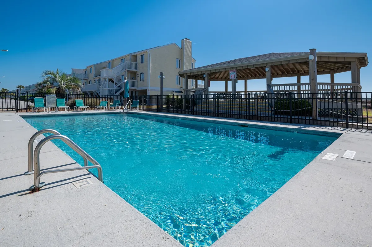 This image features a sparkling swimming pool surrounded by lounge chairs and a gazebo, set against a bright outdoor backdrop. The arrangement invites social gatherings and family relaxation, with space for sunbathing or playing by the pool.