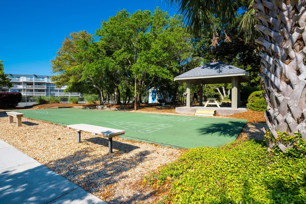 A green court area with a gazebo, benches, and shaded by surrounding trees. The space is ideal for a variety of family-friendly activities like games, picnicking, and socializing, and exudes a playful and relaxed vibe.