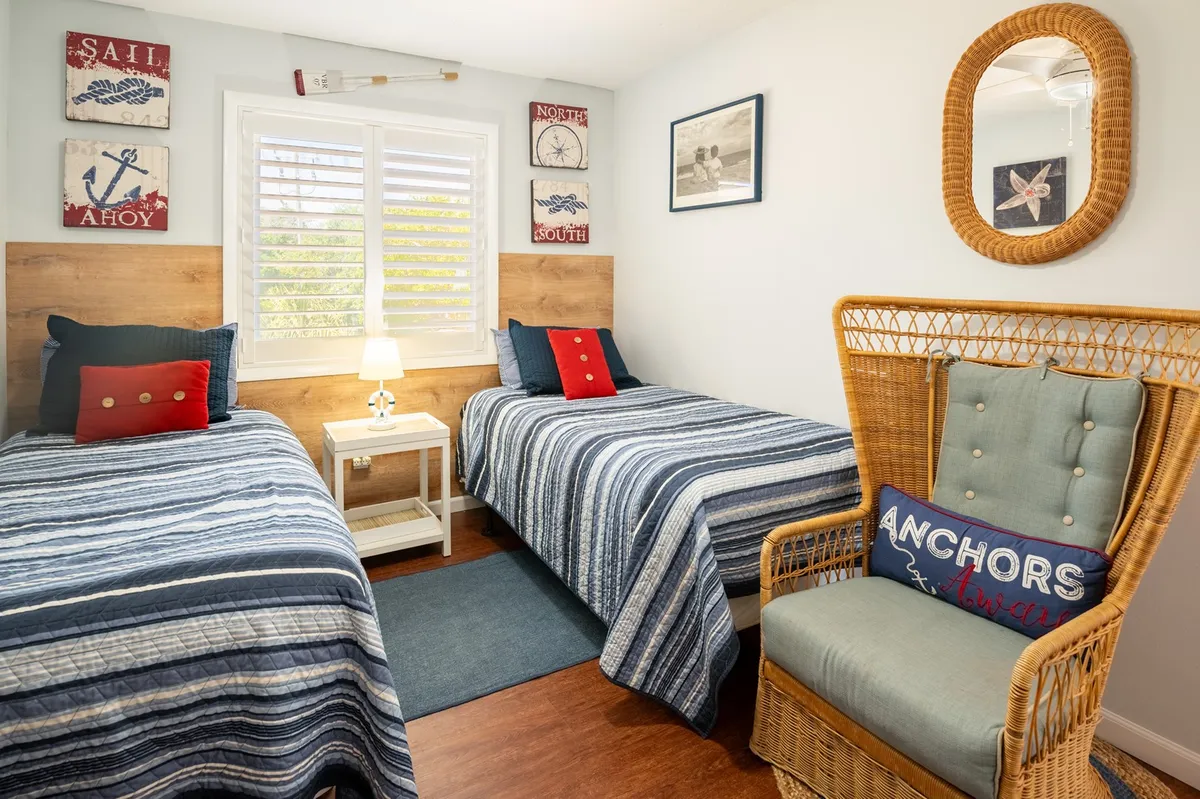 A vibrant, nautical-themed guest bedroom with two twin beds featuring striped bedding and a woven chair with cushions. Decorative wall art adds charm, and the setting feels both comfortable and tailored for kids or friends.