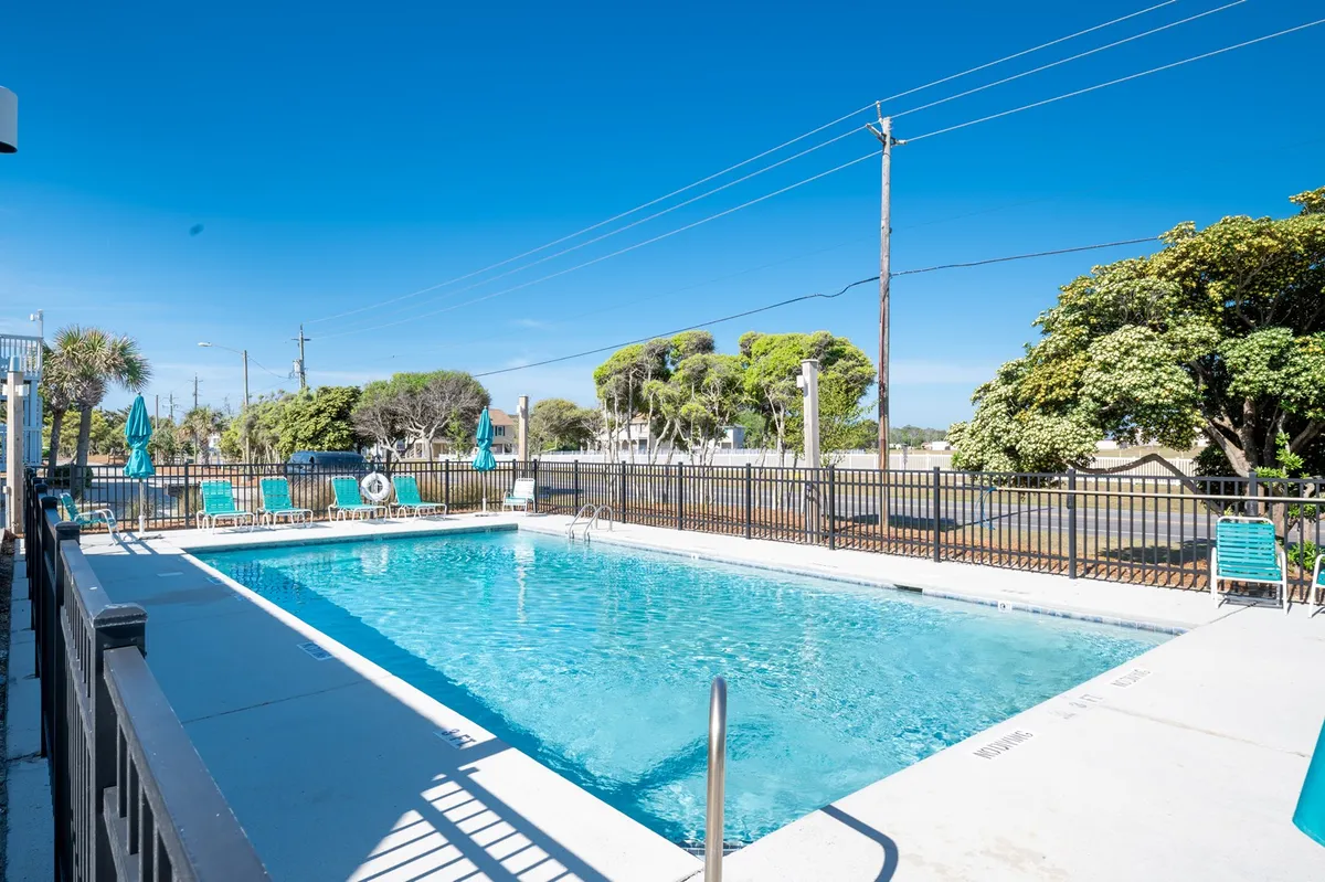 A sparkling resort-style swimming pool is surrounded by lush greenery and ample lounge chairs shaded by umbrellas. The pool area feels lively and inviting, ideal for both swimming and relaxing between activities. The scene conveys a sense of relaxation combined with the energy of social gatherings and outdoor fun.